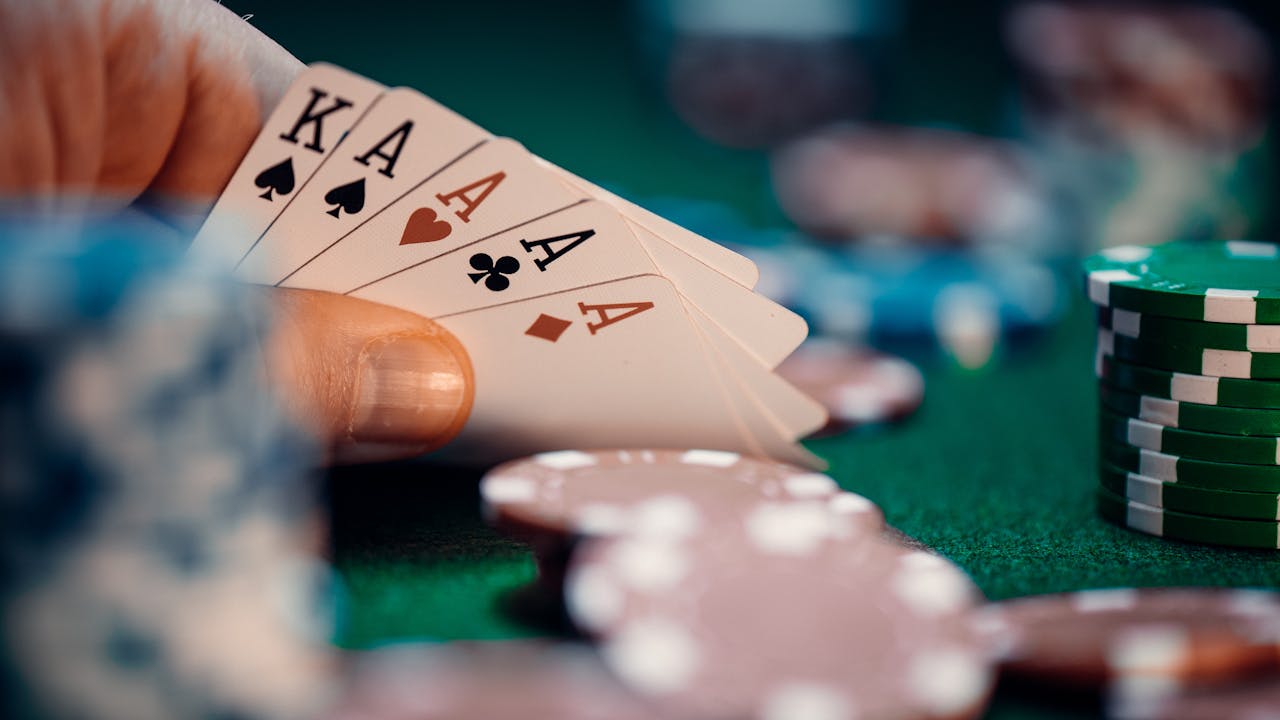 services-01 Close-up of poker hand holding four aces and kings with colorful chips on green table for high-stakes gaming.