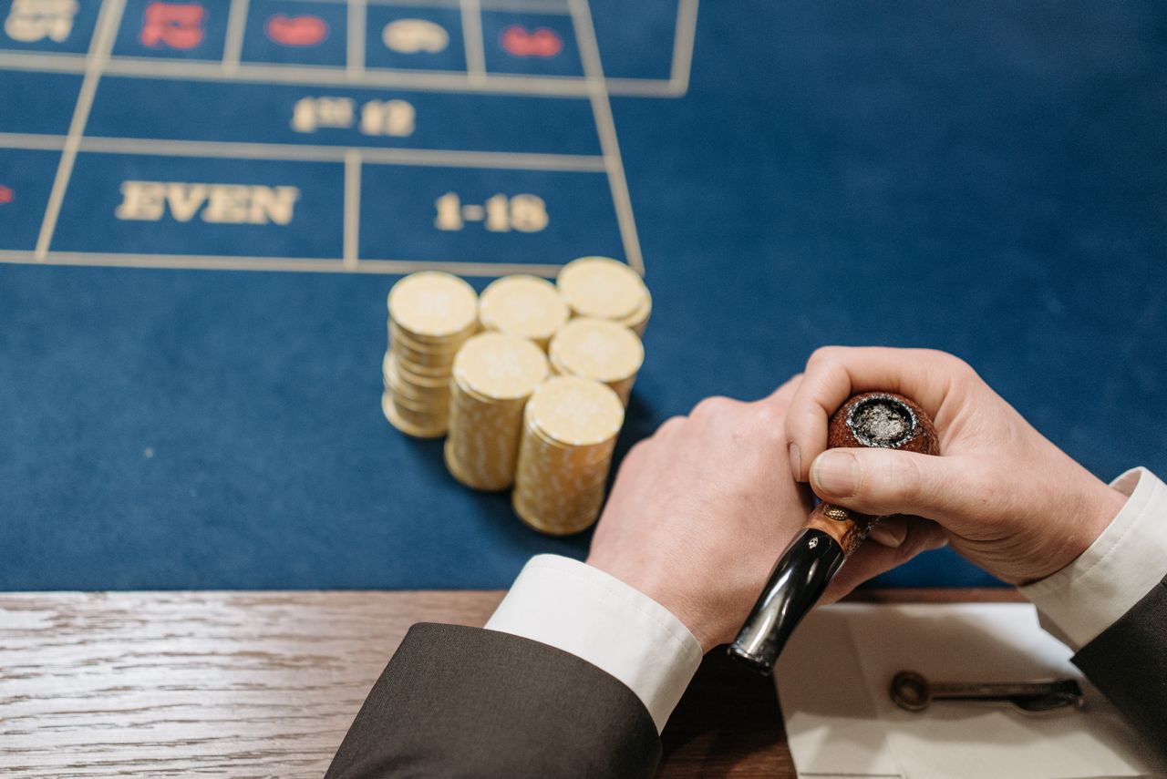 gallery-6 Hands holding a tobacco pipe and poker chips on a casino table. Top view.