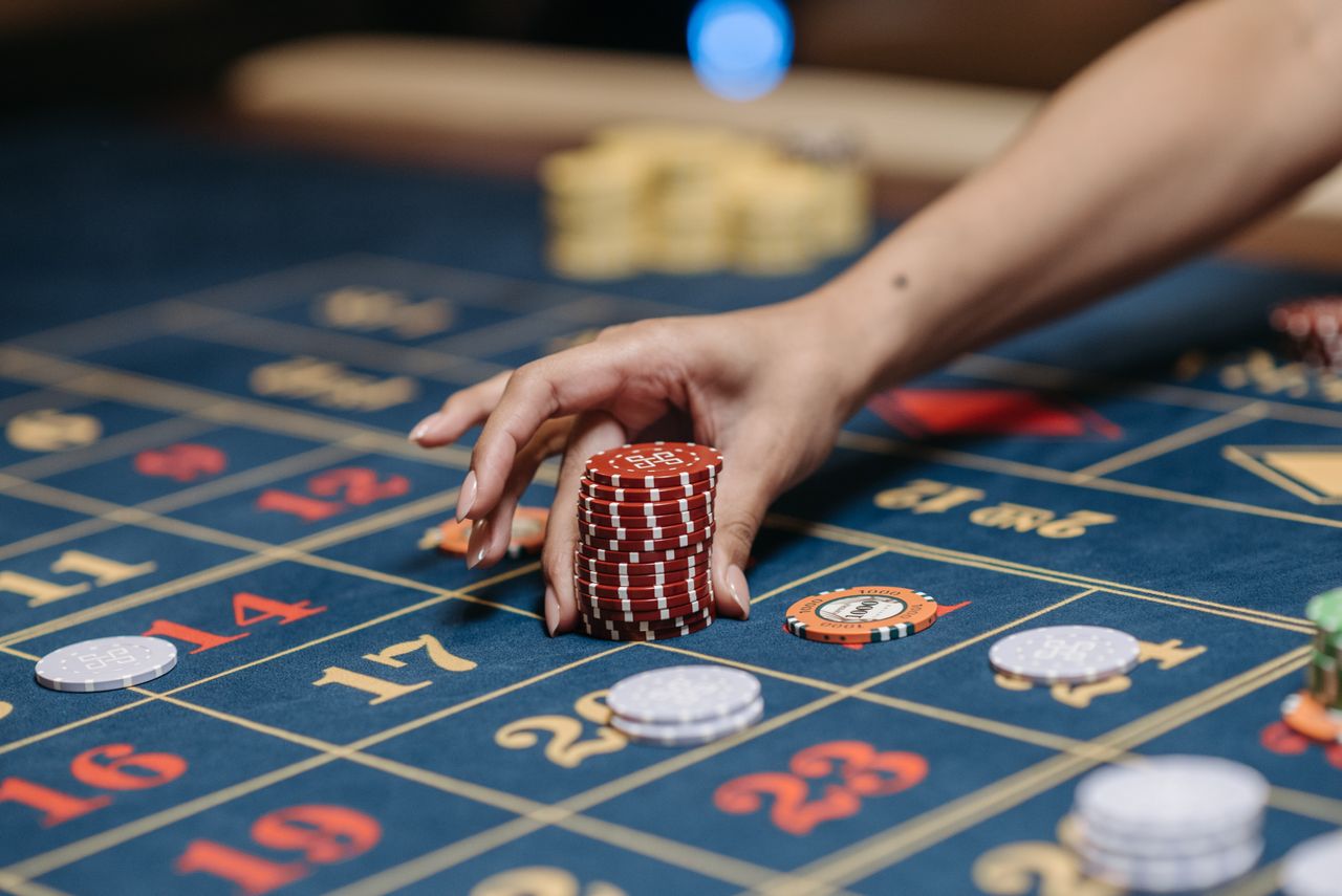 services-01 A hand holding poker chips on a roulette table, showcasing gambling and casino gaming.