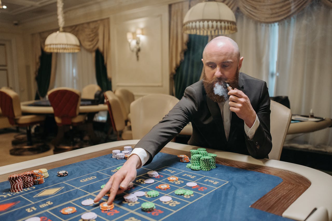 gallery-5 Bald bearded man in suit smoking pipe, bets at poker table inside luxurious casino.